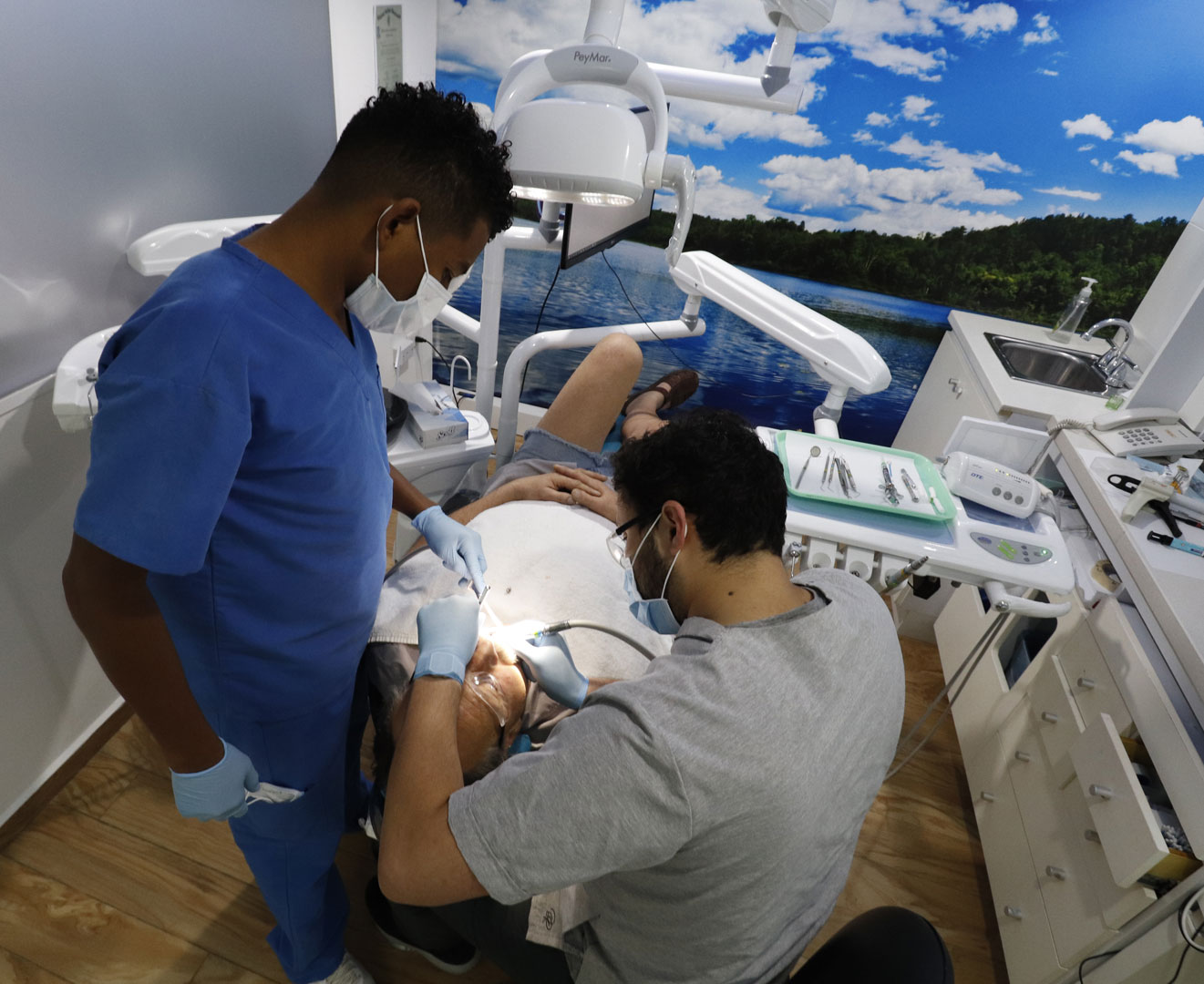 Odontólogo atendiendo a un paciente en consultorio dental, mientras la asistente limpia instrumentos clínicos